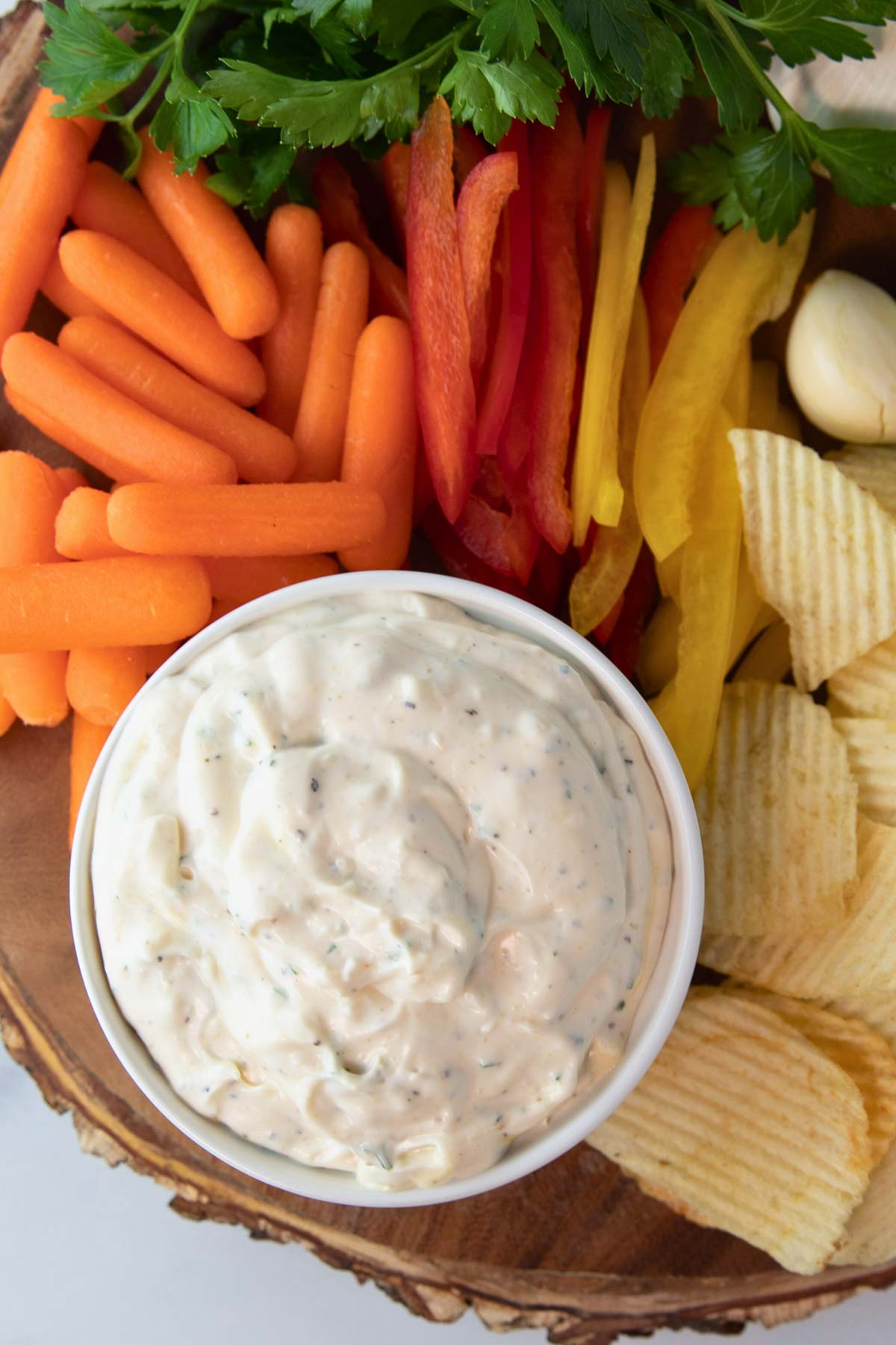 overhead of bowl of garlic dip surrounded by fresh vegetables and chips