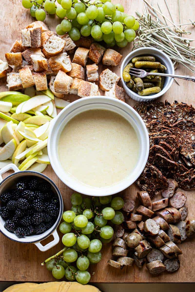 cheese fondue on platter with bread, meat, fruit, and crackers