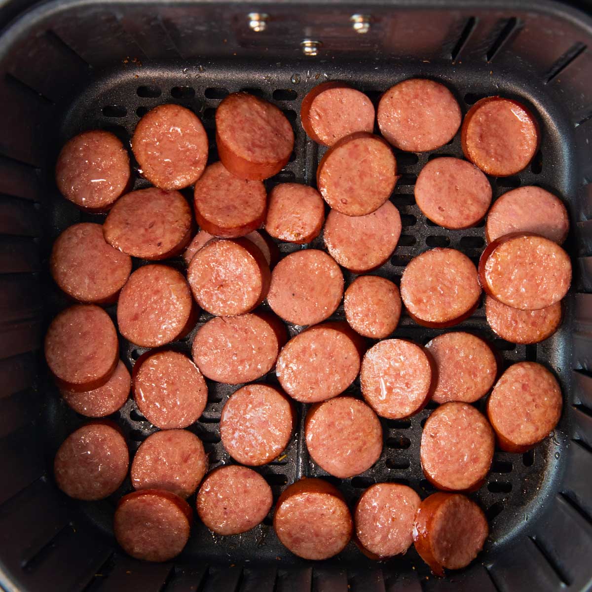 overhead of air fryer basket of sliced kielbasa sausage